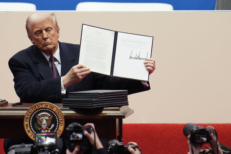 A man in a dark suit at a desk holding a folder with white pages in it.