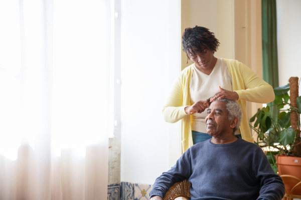 Woman brushing older man's hair by window