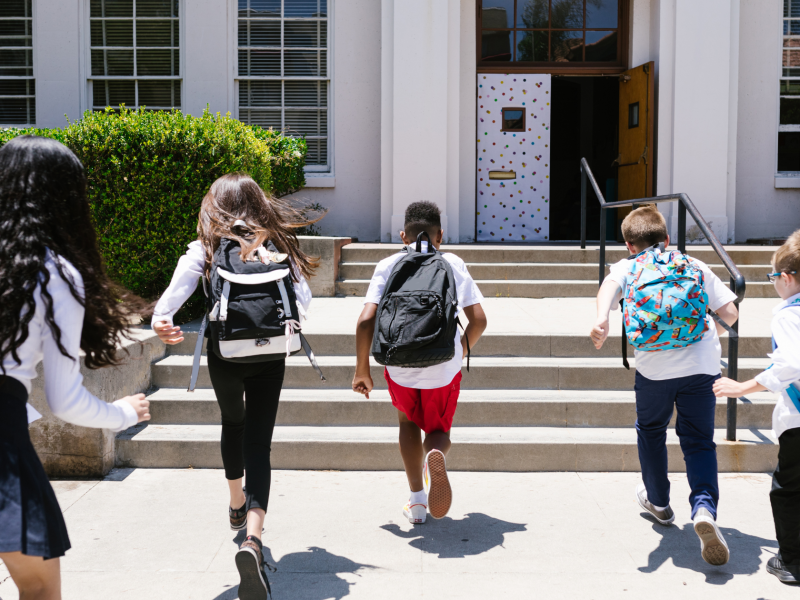 Students with backpacks running towards a school
